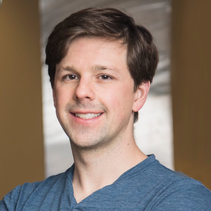 Square portrait of David Gleich indoors in a blue henley against a warm background