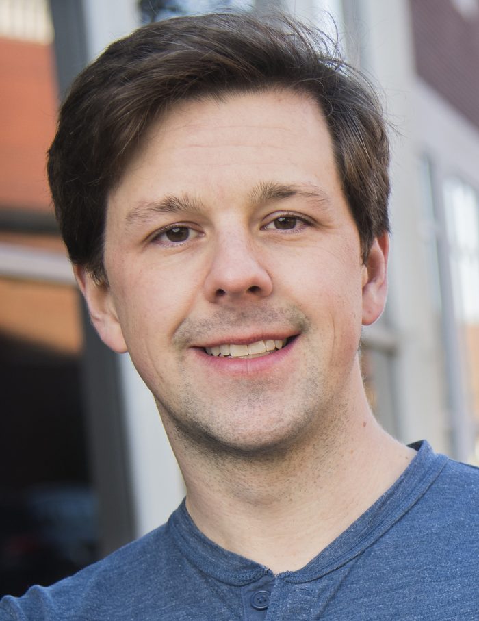 David Gleich outdoors in a blue henley, brick and windows blurred behind him