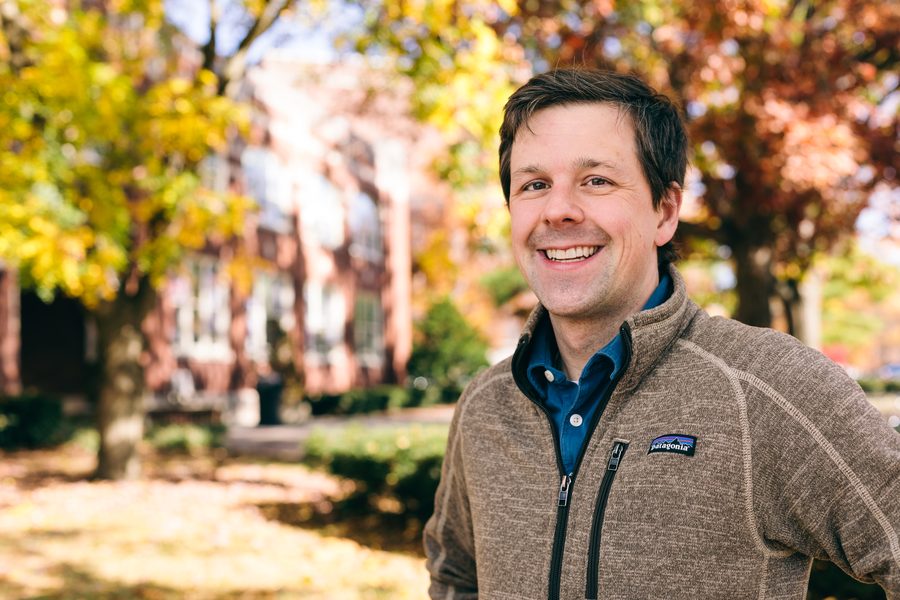 David Gleich outdoors in a fleece jacket over a blue shirt, autumn campus behind him