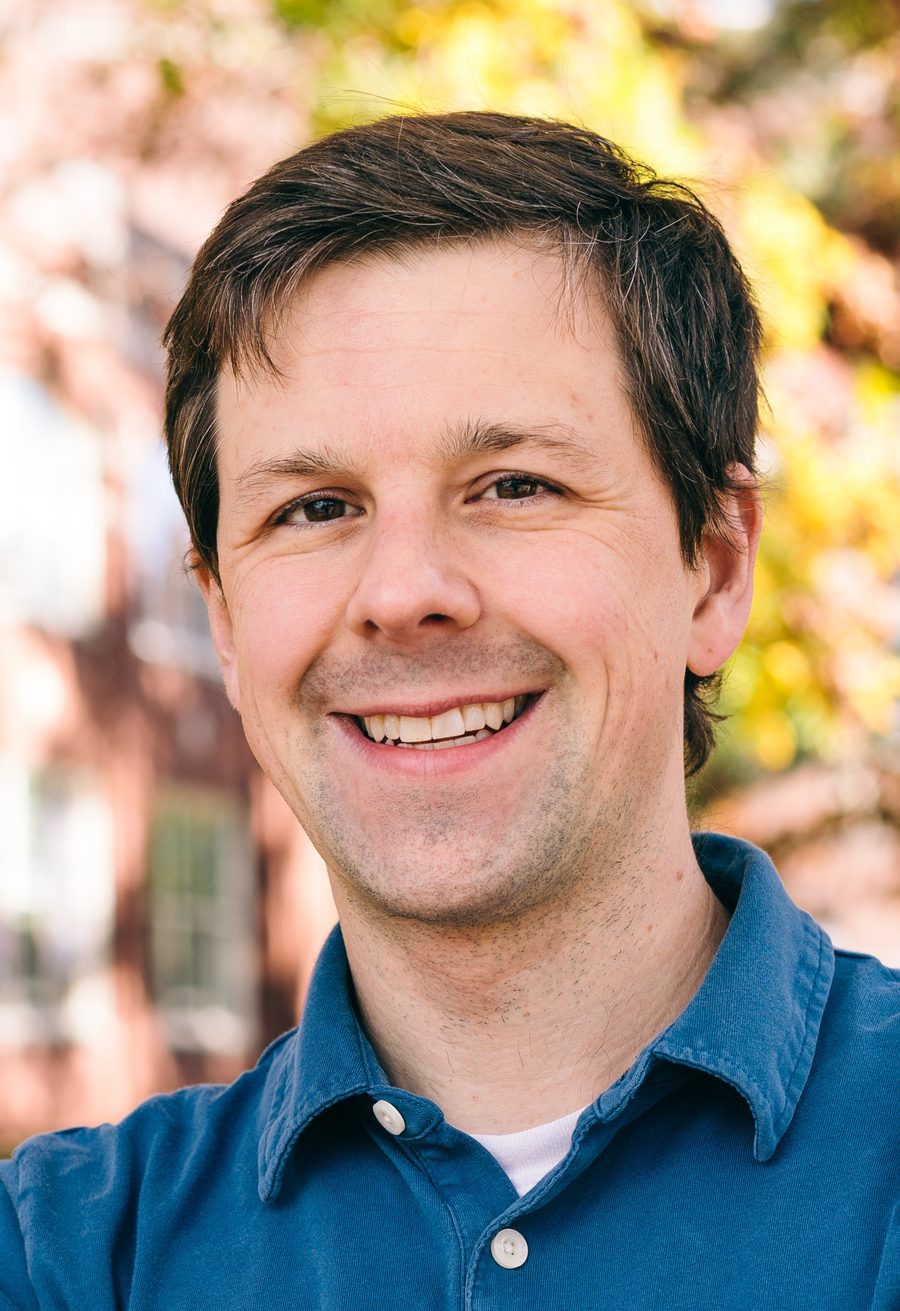 David Gleich outdoors in autumn wearing a blue shirt, with a brick building blurred behind