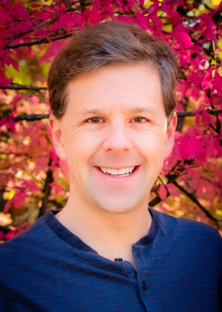 David Gleich outdoors in front of a shrub in bright red fall colour, wearing a navy henley